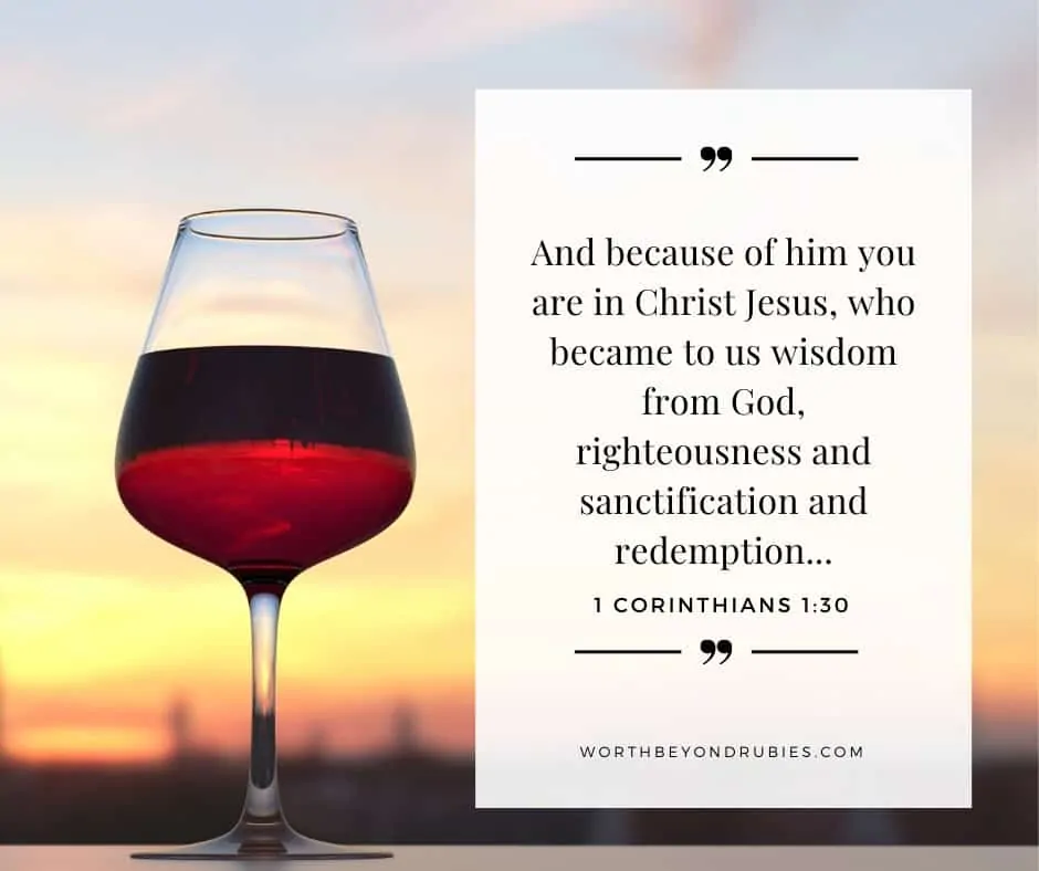 A cup of wine on a table with the sunset in the background with 1 Corinthians 1:30 on the image