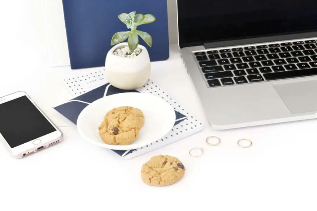 An image of a laptop on a desk with cookies on a plate next to it with one sitting on the desk and a succulent and blue accessories in the background