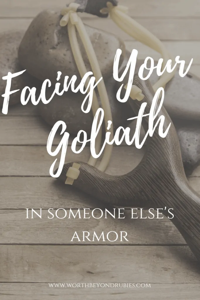 A wooden backdrop with stones and a slingshot with a text overlay that says Facing Your Goliath in Someone Else's Armor