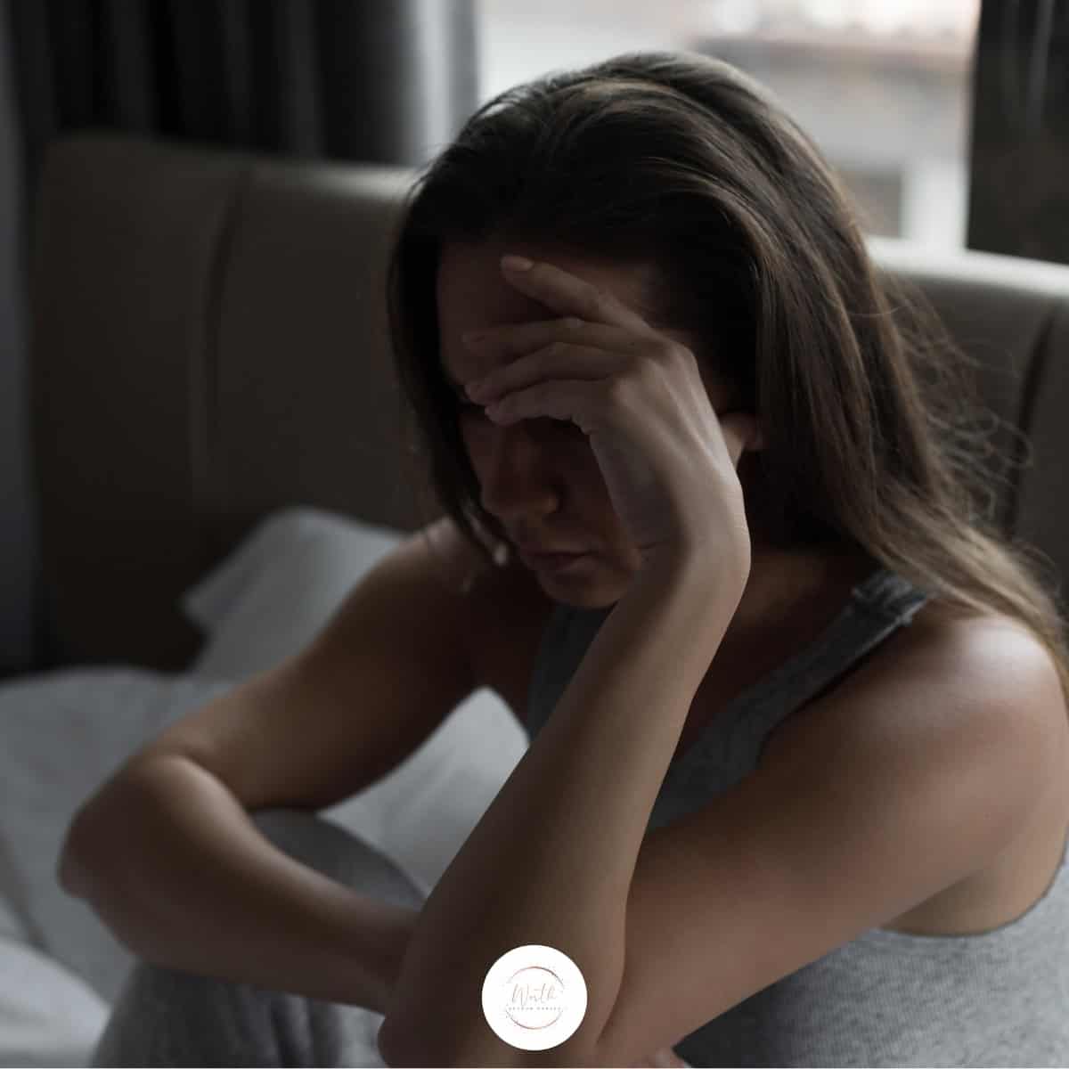 a woman sitting on a bed with her hand on her face