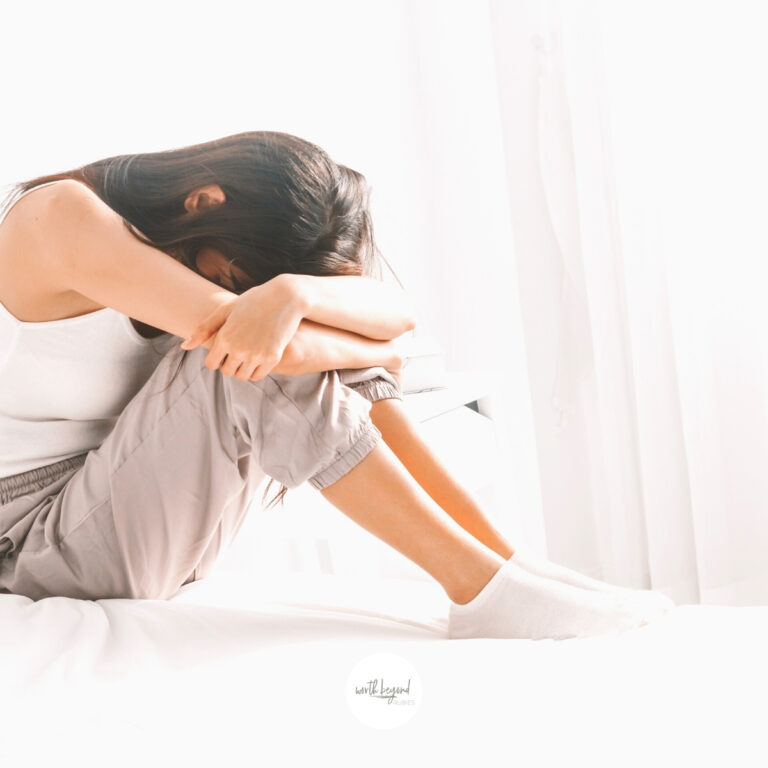 A woman on a bed in sweats with her head down on her knees for post called Overcoming Guilt From Past Mistakes