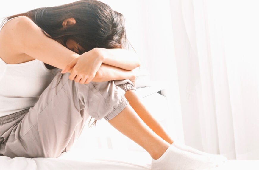 A woman on a bed in sweats with her head down on her knees for post called Overcoming Guilt From Past Mistakes