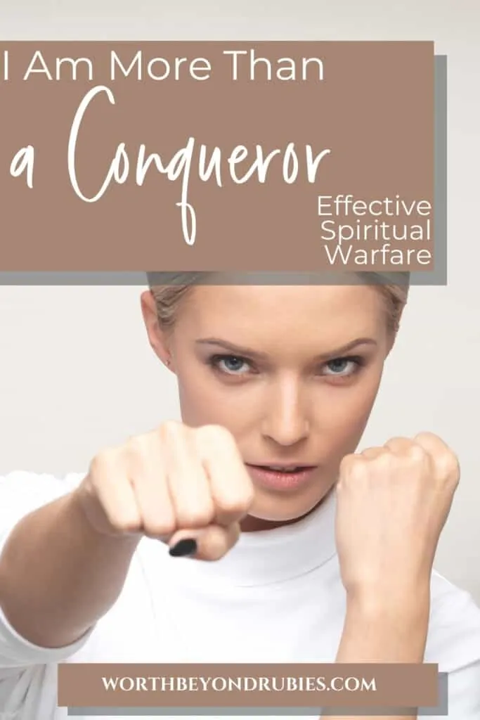 A woman with blonde hair pulled back, wearing a white shirt with one hand up guarding her face and the other hand punching as though she is boxing, and computers behind her in the background with a text overlay that says I Am More Than a Conqueror - Effective Spiritual Warfare