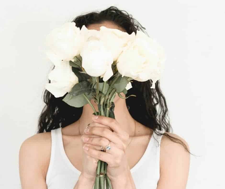 A woman in a white tank top holding white flowers up in front of her face