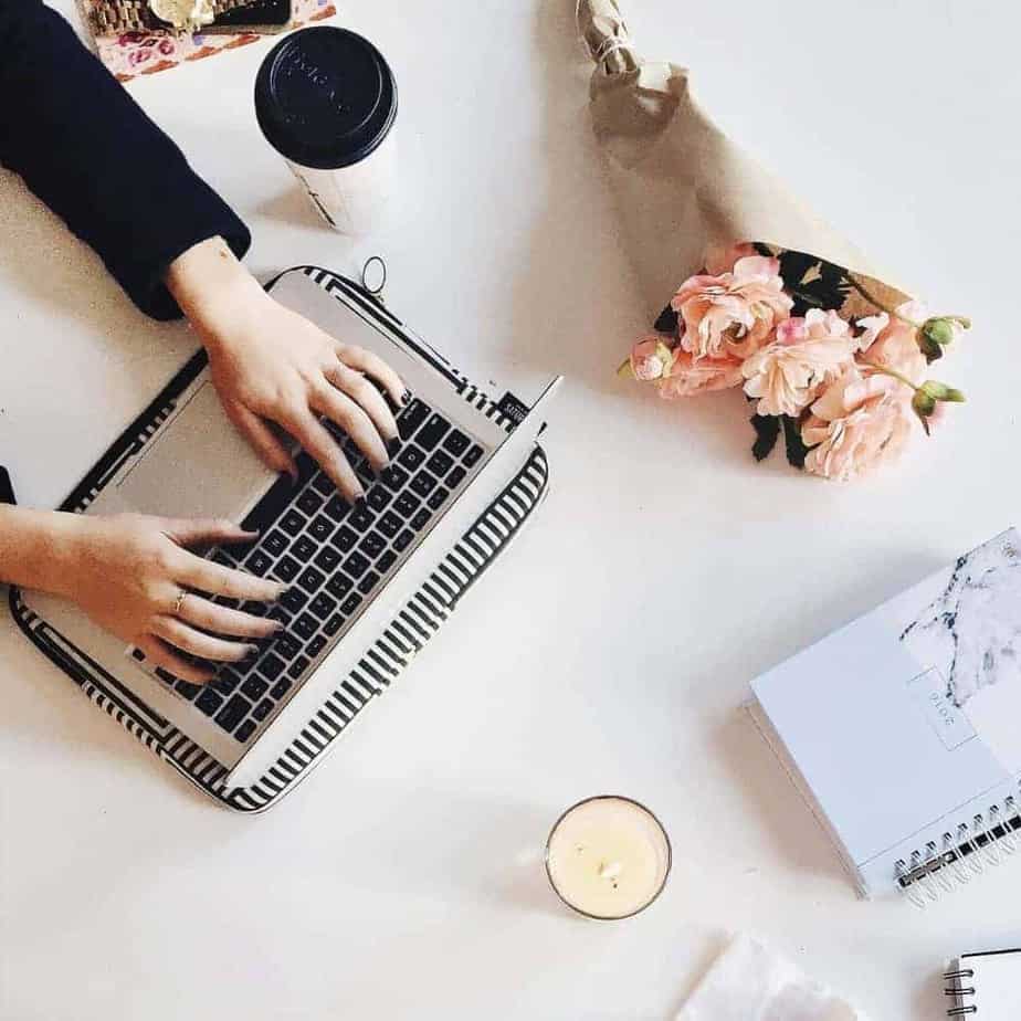 An image of laptops and a woman's hands on the keyboard of one, with coffee and various notebooks on the table