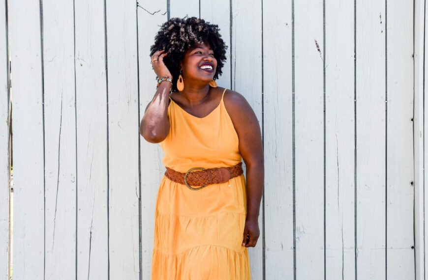 a pretty black woman in an orange dress against a wooden wall smiling for post titled How Can We Know God Hears Our Prayers - Answers to 4 Key Questions About Prayer
