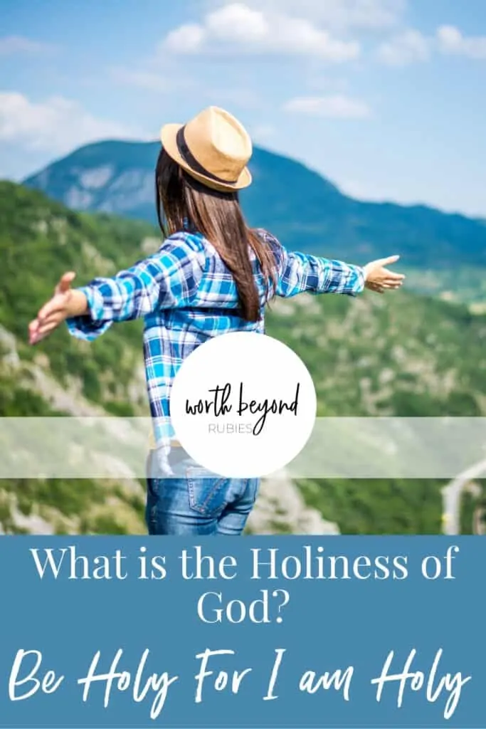 A woman with long brown hair and a blue plaid shirt and brown hat on a mountain and text that says What is the Holiness of God? - Be Holy For I Am Holy