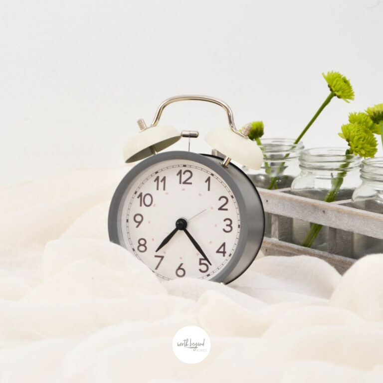 an image of an alarm clock sitting on fabric and the Worth Beyond Rubies logo at the bottom of the image