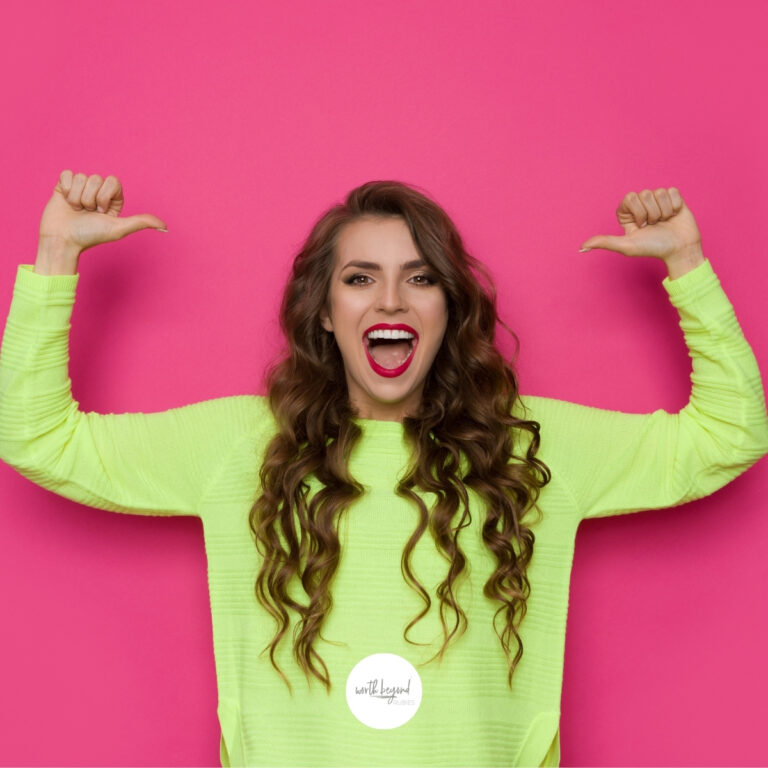 an image of a woman with long brown hair in a lime green shirt with both arms up and her thumbs pointing at her head, her mouth open in a smile for post called I Am More Than a Conqueror - Effective Spiritual Warfare and the Full Armor of God