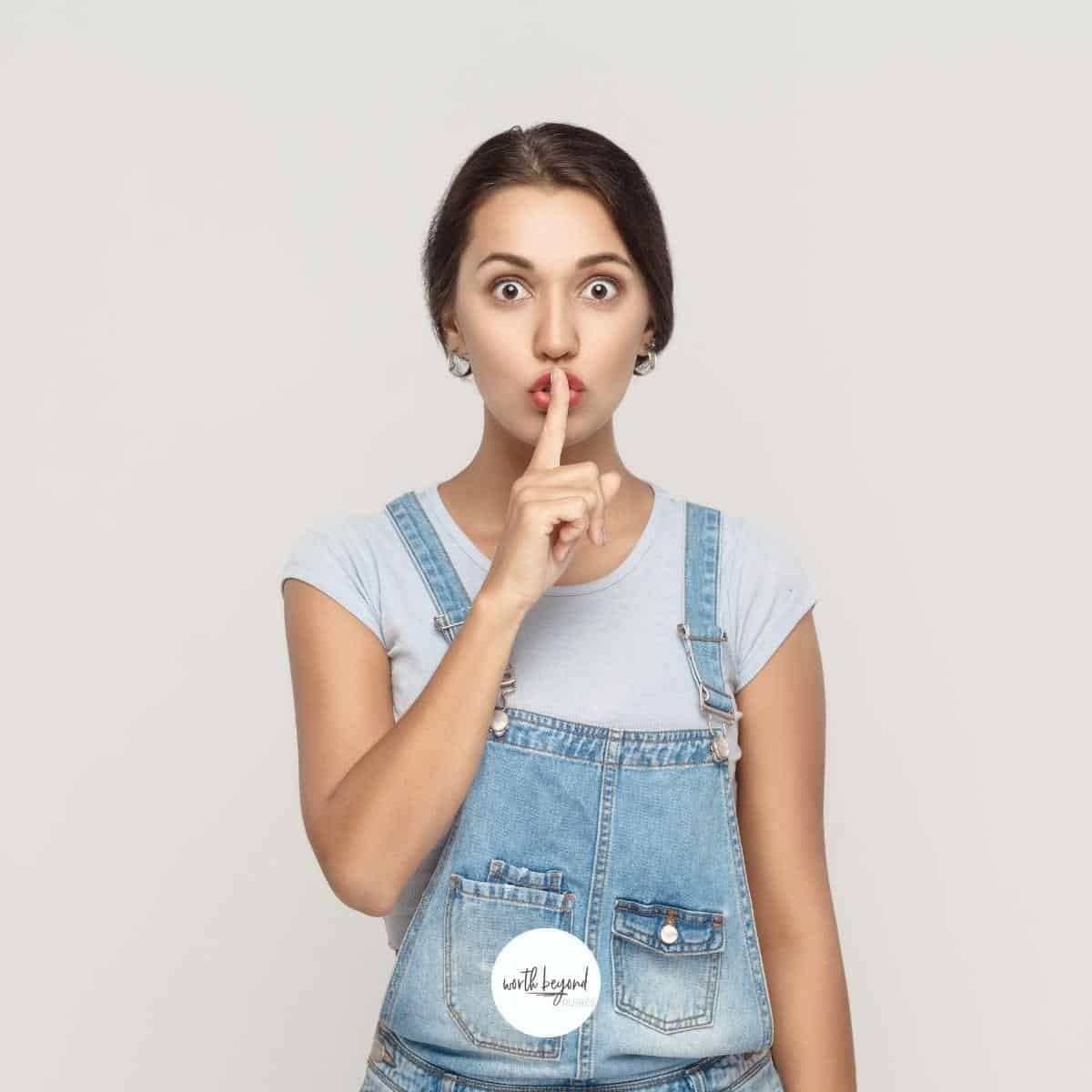 a woman with her finger over her lips to shush and the Worth Beyond Rubies logo at bottom of image - for post on how to tame your tongue