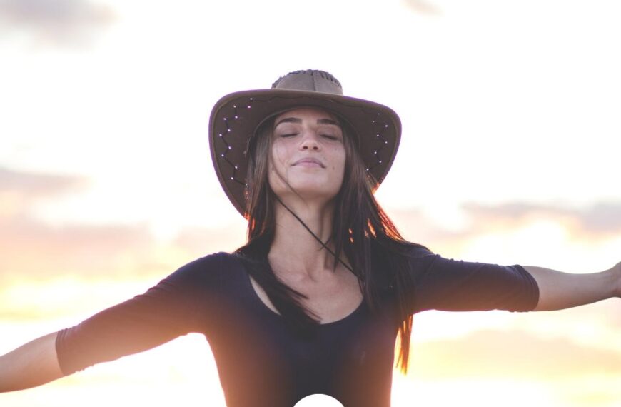 A woman in a brown sweater and a brown wide-brimmed hat at sunset standing with her eyes closed and arms outstretched and the Worth Beyond Rubies logo at the bottom of the image.