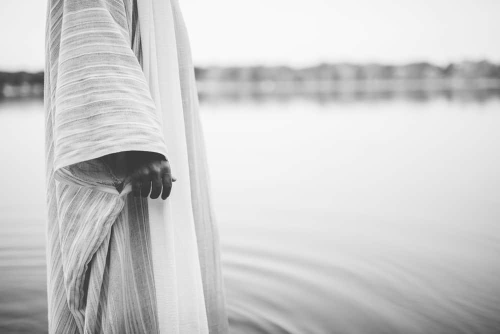 Water in the Bible: 9 Attributes and What it Symbolizes 2 A closeup shot of a person wearing a biblical robe while standing in the water in black and white; symbolism of water in the Bible