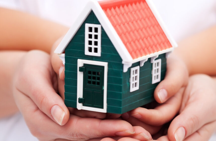 Hands holding a model of a green home and the Worth Beyond Rubies logo for post on praying over your home