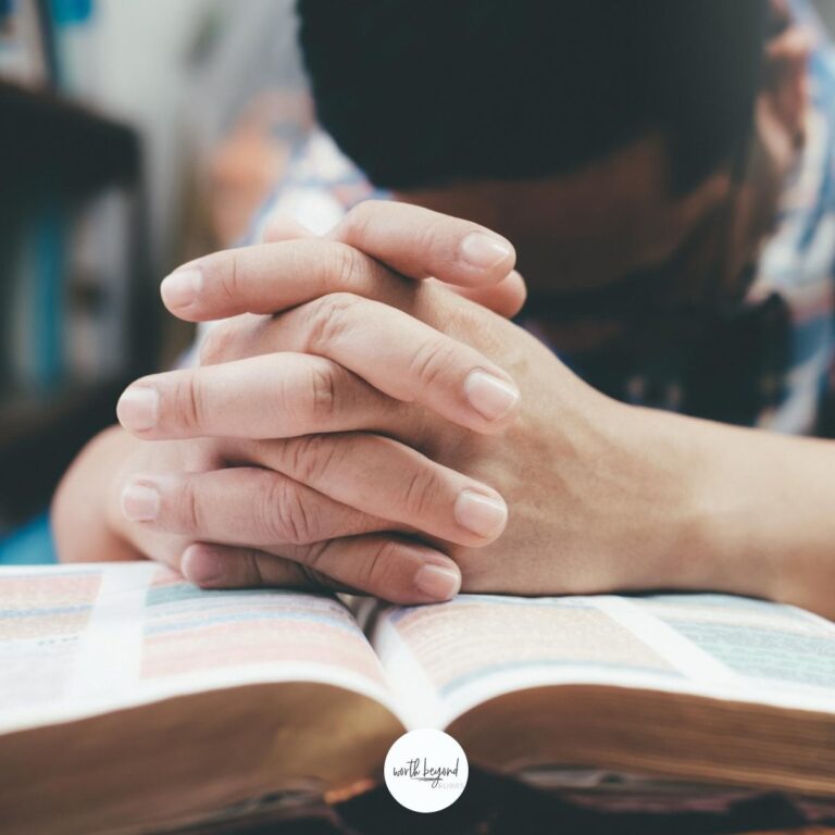 A man's hands folded in prayer on a Bible with the Worth Beyond Rubies logo at the bottom for post on how to pray according to the Bible