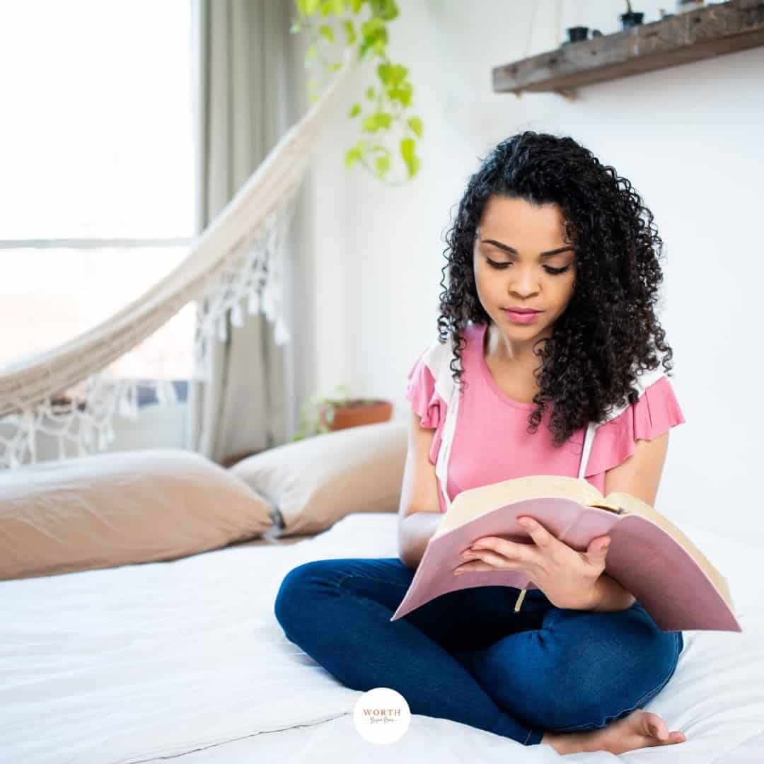 young woman sitting on bed reading Bible.